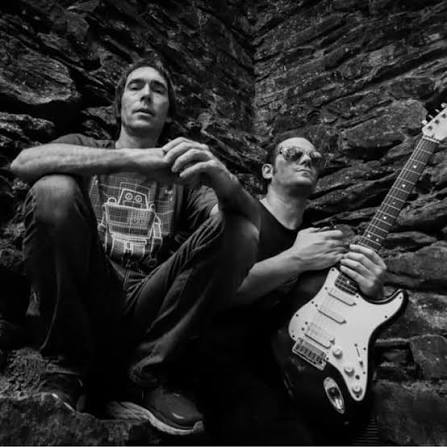 I.O.Z duo seated against a slate rock face, one holding a Stratocaster